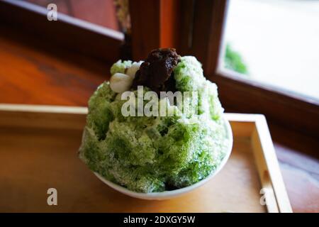 Primo piano tè verde Matcha Kakigori condito con mochi e fagioli rossi purè su tavola di legno, dessert ghiacciato giapponese rasato Foto Stock
