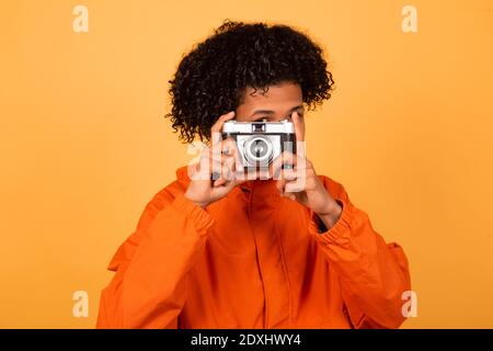 Bel giovane afroamericano in un impermeabile arancione, isolato su sfondo giallo parete, studio ritratto. Concetto di stile di vita delle persone. Spazio di copia d Foto Stock