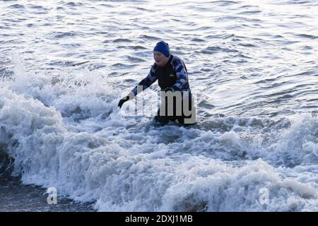 West Bay, Dorset, Regno Unito. 24 dicembre 2020. Regno Unito Meteo. Un nuotatore emerge dal mare dopo un tuffo di mattina presto presso la spiaggia all'alba a West Bay in Dorset su una fredda, chiara mattina di sole la vigilia di Natale. Picture Credit: Graham Hunt/Alamy Live News Foto Stock