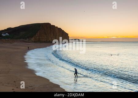 West Bay, Dorset, Regno Unito. 24 dicembre 2020. Regno Unito Meteo. Un nuotatore emerge dal mare dopo aver fatto un tuffo di mattina presto presso la spiaggia all'alba a West Bay in Dorset in una fredda e chiara mattina soleggiata la vigilia di Natale. Picture Credit: Graham Hunt/Alamy Live News Foto Stock