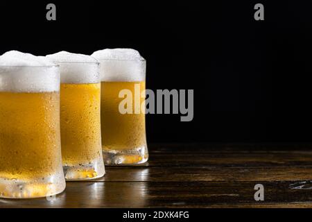 Tre tazze di birra ghiacciate su base di legno su sfondo nero con spazio per la copia. Messa a fuoco selettiva. Foto Stock