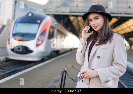 Ritratto di giovane bella donna alla stazione ferroviaria che parlare al telefono Foto Stock