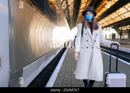 Donna turistica mascherata alla stazione ferroviaria. Turismo durante un concetto pandemico. Misure di prevenzione dei virus nei trasporti pubblici Foto Stock