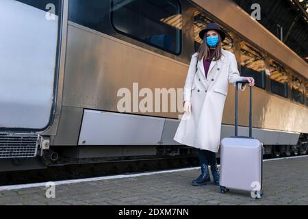 Donna turistica mascherata alla stazione ferroviaria. Turismo durante un concetto pandemico. Misure di prevenzione dei virus nei trasporti pubblici Foto Stock