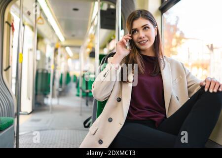 Il passeggero femminile si siede sul tram e parla al telefono. Bella donna caucasica a cavallo nei mezzi pubblici Foto Stock