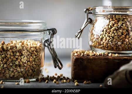 Groat di grano saraceno verde senza cottura in vaso di vetro, cibo vegetariano sano su tavolo da cucina grigio, spazio copia, fuoco selettivo Foto Stock