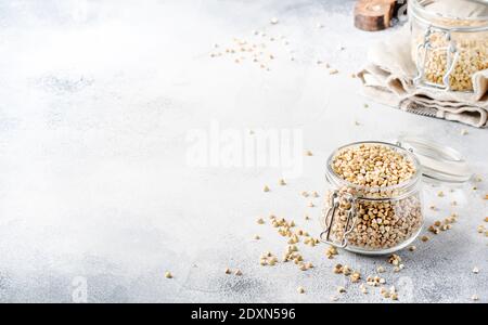 Groat di grano saraceno verde senza cottura in vaso di vetro, cibo vegetariano sano su tavolo da cucina grigio, spazio copia, fuoco selettivo Foto Stock