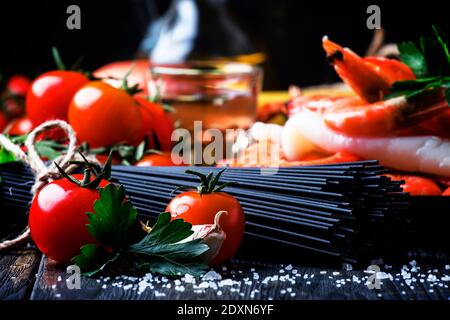 Spaghetti neri, pomodori ciliegini, vino bianco, gamberetti, calamari, vita morta in basso, fuoco selettivo Foto Stock