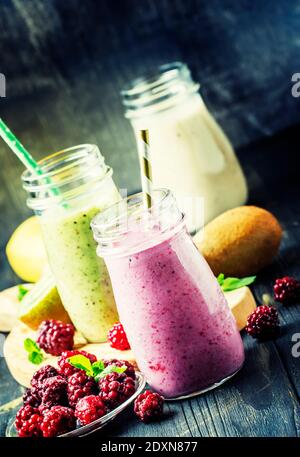 Frullati multicolore di frutti di bosco e frutta, assortiti in bottiglie di vetro, fuoco selettivo Foto Stock