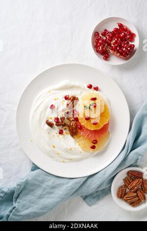 Ricotta con agrumi, noci pecan e miele su piatto bianco su tavola bianca. Verticale, vista dall'alto Foto Stock