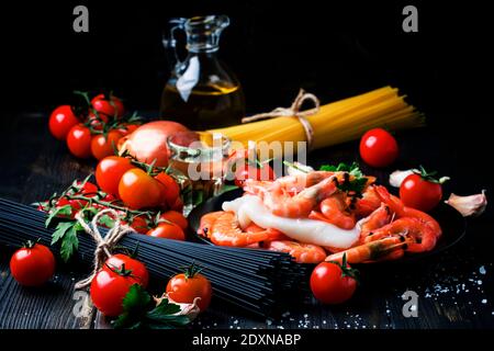 Spaghetti neri, pomodori ciliegini, vino bianco, gamberetti, calamari, vita morta in basso, fuoco selettivo Foto Stock