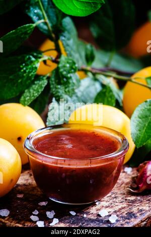 Salsa di prugna alla ciliegia georgiana Tkemali, con aglio, fondo ligneo vintage, fuoco selettivo Foto Stock