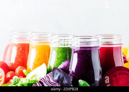 Succhi e frullati di verdure vegan multicolore in bottiglie di vetro su tavola grigia, fuoco selettivo Foto Stock