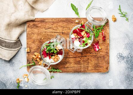 Insalata di barbabietole con rucola fresca, formaggio di capra morbido e noci, barattolo di insalata alla moda, forchetta in acciaio, fondo grigio tavola da cucina, tagliere in legno, copia s Foto Stock