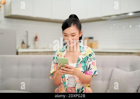 Felice millenario ispanica ragazza teenager controllare i social media tenendo smartphone a casa. Foto Stock