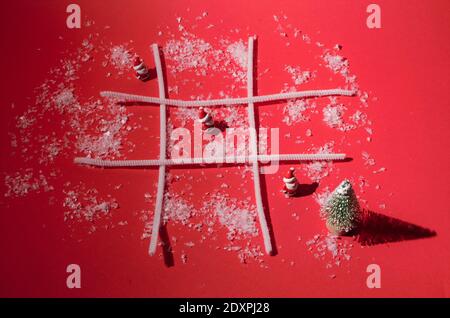 Concetto festivo minimo: tic tac TOE game con tre Babbo Natale e un albero di Natale su sfondo rosso. Foto Stock