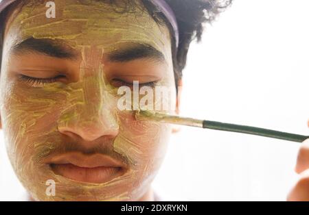 Ragazzo che si applica con maschera di fango di creta di pennello Foto Stock