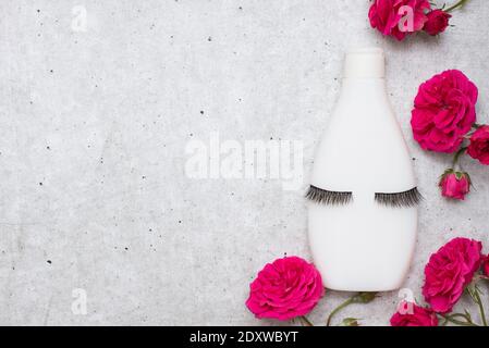 Bottiglia bianca per shampoo e cosmetici con false ciglia e. fiori rossi su sfondo grigio con spazio per la copia Foto Stock