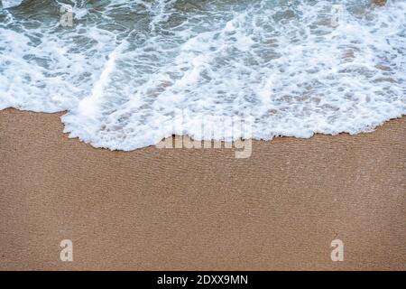 L'onda dell'oceano viene sulla sabbia. Vista ravvicinata dall'alto. Texture per lo sfondo. Spazio di copia per il testo Foto Stock