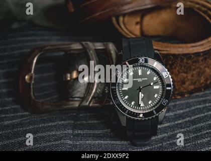 Primo piano di un orologio cromato nero, una fibbia per cintura di una cintura in pelle e parte di un bracciale in pelle sopra il tessuto grigio Foto Stock