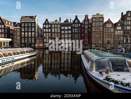 Amsterdam, Paesi Bassi 16 dicembre 2020: Immagine del canale Damrak e dei vecchi magazzini con in primo piano le barche turistiche. Foto Stock