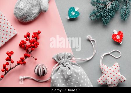 Regali naturali sostenibili per Natale zero rifiuti.Guanti, giocattoli morbidi, pioli di legno e bacche naturali. Sfondo di carta rosa a strati grigio. Foto Stock