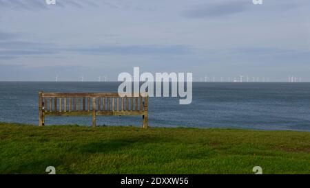 Panca vuota su erba rivolta vedere con turbine eoliche all'orizzonte Foto Stock