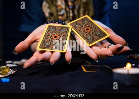 Cartomanzia. Il cassiere di fortuna tiene fuori due carte Tarocchi sulle sue palme. Primo piano. Il concetto di divinazione, astrologia ed esoterismo. Foto Stock