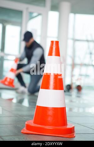 lavoratore mettendo coni intorno alla zona di umidità su pavimento piastrellato Foto Stock