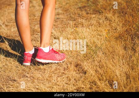 Le gambe della donna runner con le sneakers rosa camminano sul erba soleggiata e gialla in una giornata estiva nel sera Foto Stock