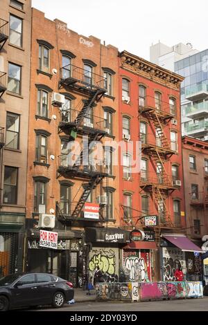 Clock Work PunkRock n roll bar insieme ad altri negozi su Essex Street, sul lato Lower East di Manhattan. Vecchi tendament come walkup con fuoco scappa giù la parte anteriore. Foto Stock