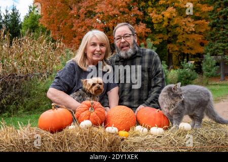 Felice anziano giovane coppia boomer pone in una scena autunnale con un cane e delle zucche Foto Stock