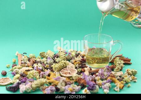 Tè alle erbe versare in una tazza di vetro, su sfondo verde tra erbe secche rosehip rosehip chamomilla curcuma, fuoco selettivo. Foto Stock