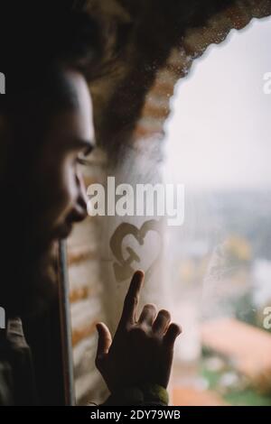 L'uomo disegnando con il dito un cuore nella finestra bagnata Foto Stock