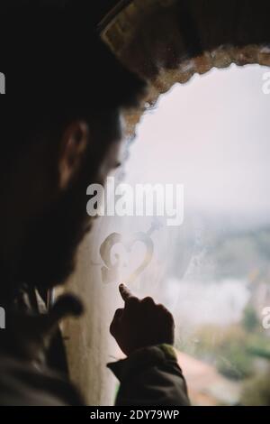 L'uomo disegnando con il dito un cuore nella finestra bagnata Foto Stock