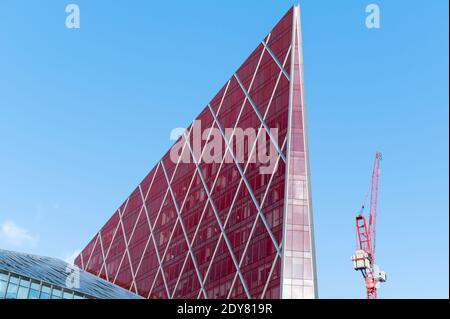 Si affaccia su di un moderno edificio d'uffici di colore rosso lucido e contemporaneo contro un cielo blu con piccole nuvole e una gru Foto Stock