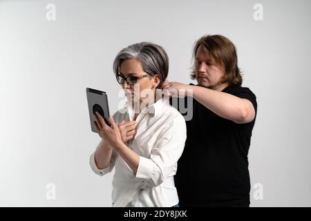 L'uomo stilista regola il costume del presentatore o del blogger prima di andare in TV, una donna adulta legge il testo utilizzando un tablet digitale isolato su Foto Stock