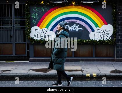 Londra, Regno Unito. 24 Dic 2020. Una donna che cammina oltre il soggiorno Avviso Salva vite arcobaleno Accedi Soho durante la vigilia di Natale 2020. Credit: SOPA Images Limited/Alamy Live News Foto Stock