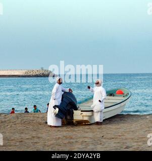 Uomini Omani in piedi presso la loro barca da pesca a sur, Oman. Foto Stock