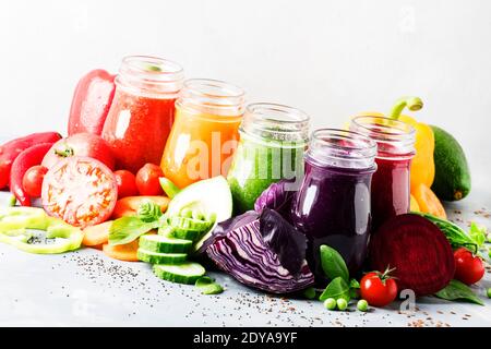 Succhi e frullati di verdure vegan multicolore in bottiglie di vetro su tavola grigia, fuoco selettivo Foto Stock