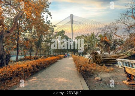 Parco pubblico joggers con fogliame autunnale e vista di Vidyasagar Ponte di cavo Setu a Princep ghat Kolkata India all'alba Foto Stock