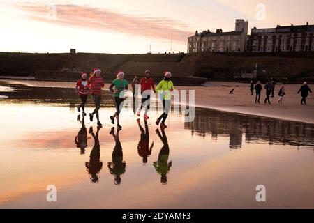I joggers prendono una corsa di Natale di mattina presto lungo la spiaggia di Tynemouth sulla costa nordorientale dell'Inghilterra. Foto Stock