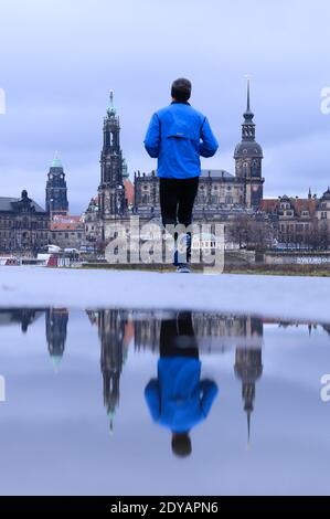Dresda, Germania. 25 Dic 2020. Un uomo cammina lungo le rive dell'Elba sullo sfondo della città vecchia e si riflette in una pozza. Credit: Sebastian Kahnert/dpa-Zentralbild/dpa/Alamy Live News Foto Stock
