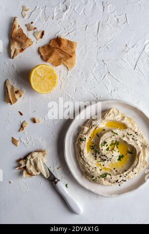 Vista dall'alto di un piatto di hummus con libanese pane piatto e limone su sfondo bianco Foto Stock