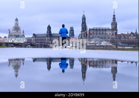 Dresda, Germania. 25 Dic 2020. Un uomo cammina lungo le rive dell'Elba sullo sfondo della città vecchia e si riflette in una pozza. Credit: Sebastian Kahnert/dpa-Zentralbild/dpa/Alamy Live News Foto Stock