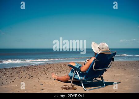 Una donna solitaria seduta sul lettino sulla spiaggia, luogo perfetto per ammirare il bel mare Foto Stock