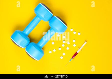 Doping nello sport. Steroidi anabolizzanti. Farmacia sportiva. Manubri di plastica, siringa, pillole su sfondo giallo. Vista dall'alto. Foto Stock