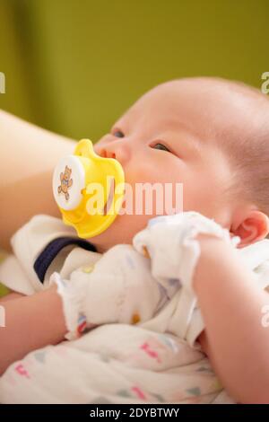 Neonato bambina cinese di meno di un mese succhiando felicemente sul suo succhietto. Foto Stock
