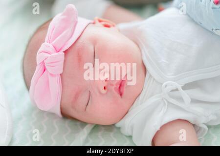 Neonato bambina cinese appena un mese vecchio dormendo sonoramente con nastro rosa sulla sua testa. Foto Stock