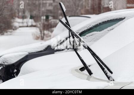 Auto innevate con tergicristalli rialzati in un parcheggio coperto di neve in una zona residenziale urbana Foto Stock